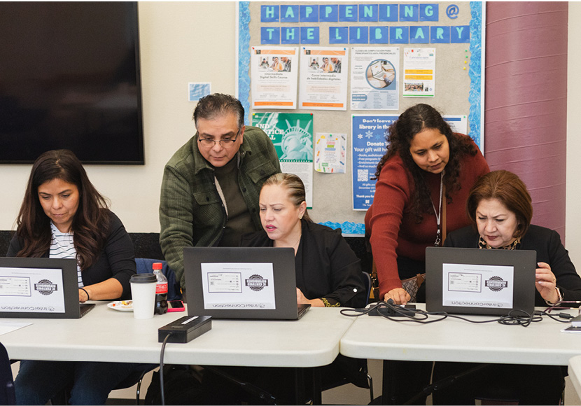 Three people sitting in front of laptop computers with two people advising.